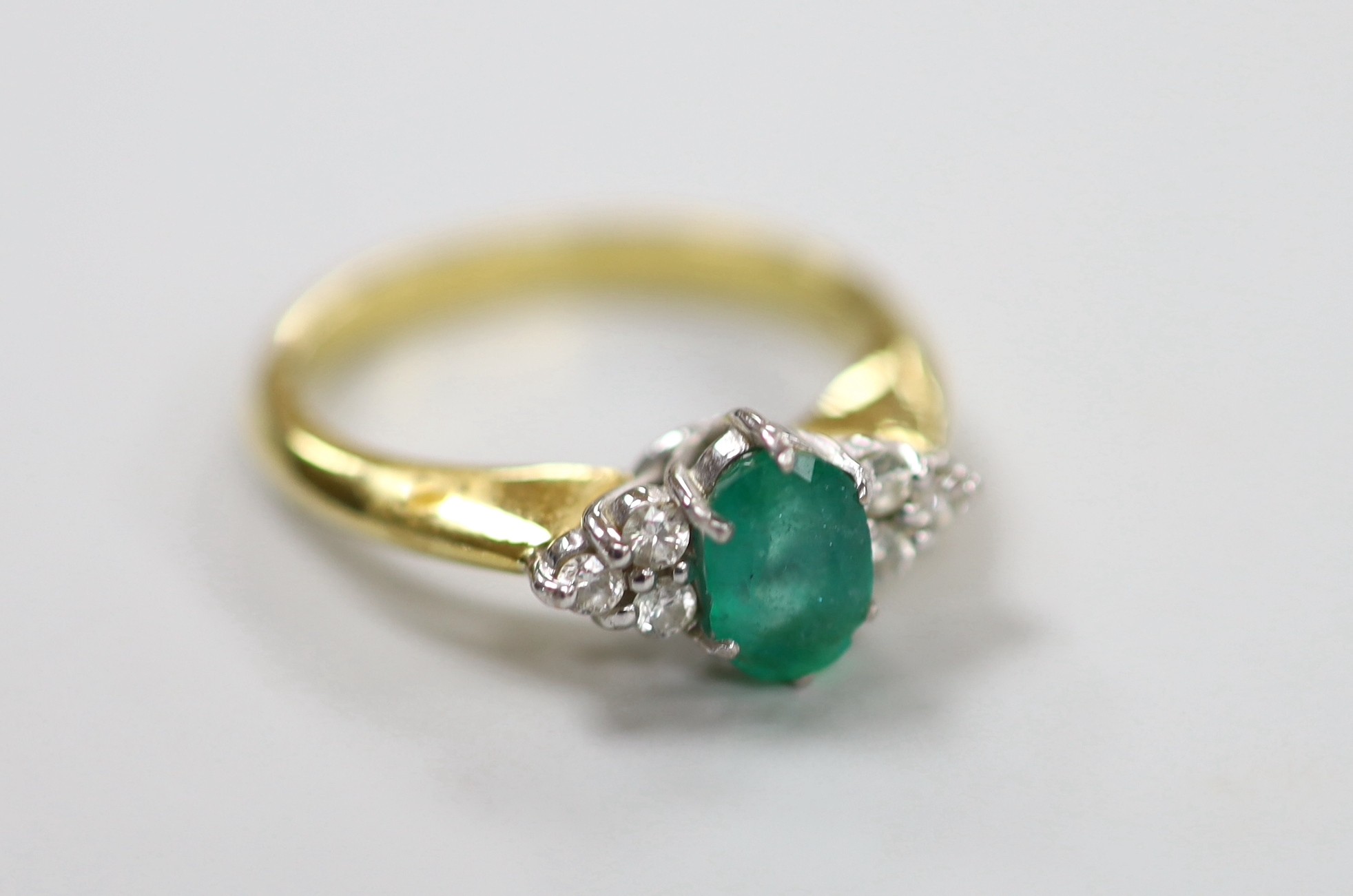 A modern 18ct gold and single stone oval cut emerald set ring, with six stone diamond chip set shoulders, size N/O, gross weight 4.8 grams.
